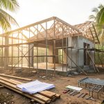 Maison en chantier sous un climat tropical aux Antilles, avec échafaudages, outils et plans au sol, entourée d’une végétation luxuriante.