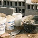 Seaux de ciment et de sable disposés avec un bac de mortier gris, une truelle et des parpaings sur un chantier.