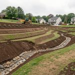 Terrain en pente nivelé avec des courbes douces, des noues végétalisées et un canal empierré permettant à l’eau de pluie de s’écouler naturellement.